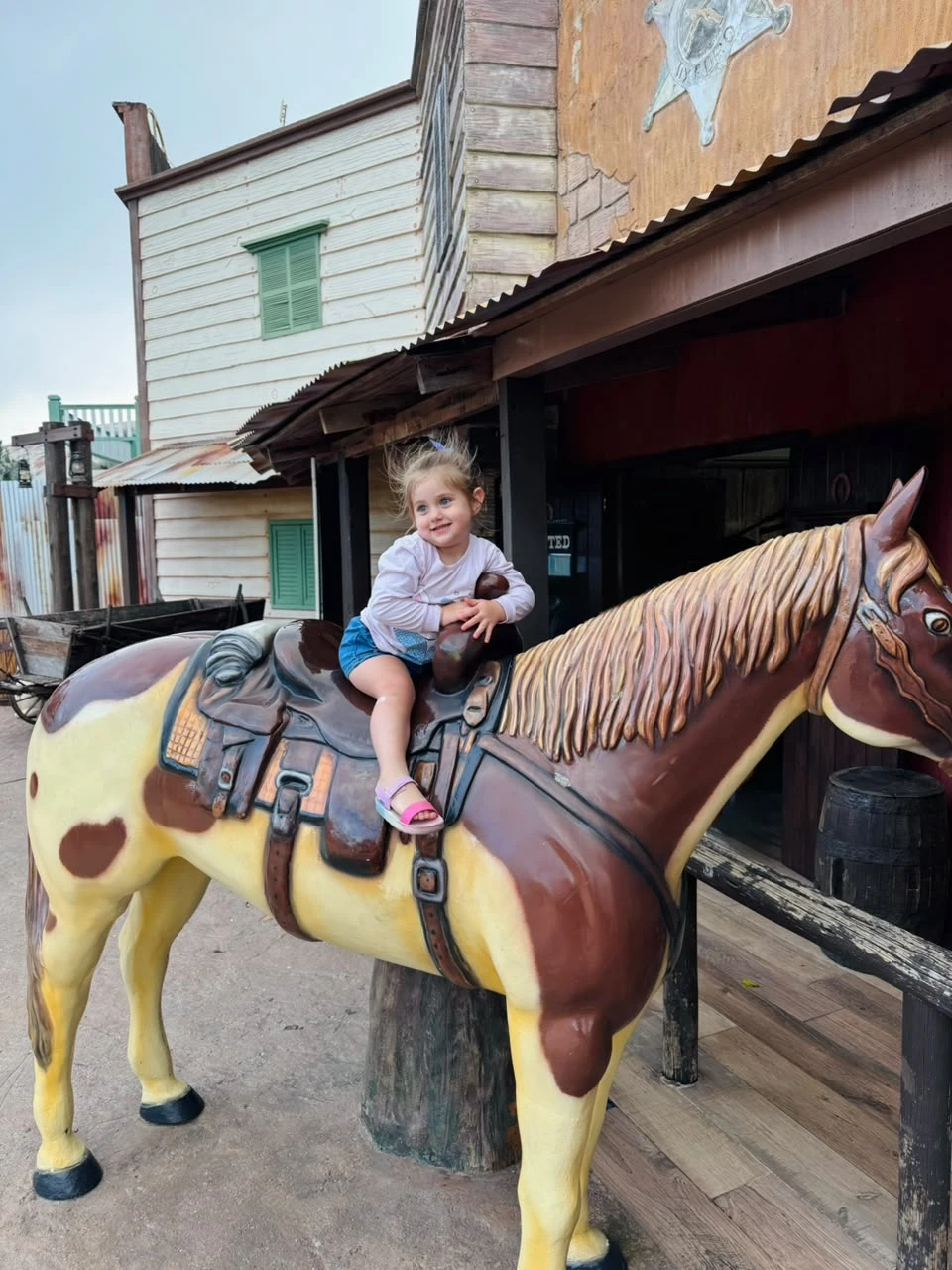 Foto original: menina sentada num cavalinho de faroeste
